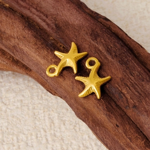 Two golden stainless steel starfish charms for DIY jewelry making on a wooden surface