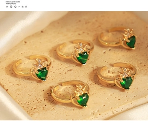 Primo piano di anelli a corona dorati con zircone verde a cuore su vassoio