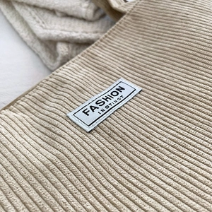 Detailed close-up of beige corduroy fabric texture and Fashion Instinct label on bag