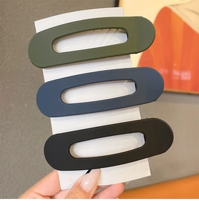 Three matte hair clips in olive green, dark blue, and black with hollow oval design