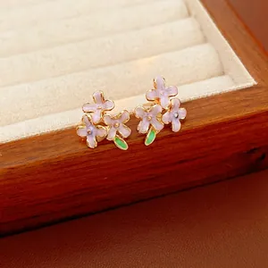 Elegante lila Flieder Ohrringe mit goldenem Rand und grünem Blattdetail in einer Schmuckschatulle