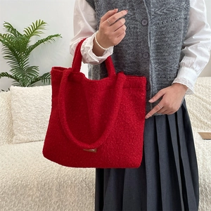 Detail of red plush tote bag being held by a model in a cozy indoor setting