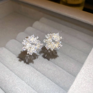 Macro shot of silver needle snowflake stud earrings with crystals and pearls in a velvet box