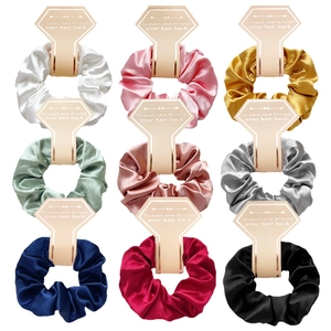 Close-up of nine colorful satin scrunchies with elegant heart-shaped labels on white background