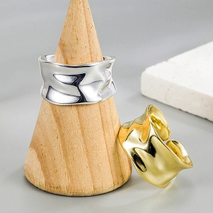Close-up of gold and silver irregular wavy rings displayed on a wooden stand
