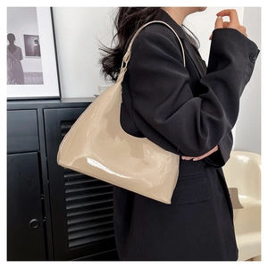 Close-up of beige patent leather shoulder bag with glossy finish on a black blazer