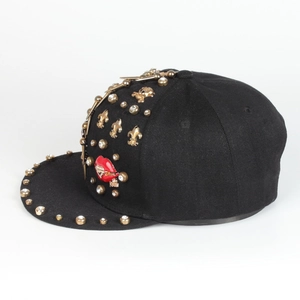 Detail of black snapback hat with gold rivets, fleur-de-lis and red lip badge decoration