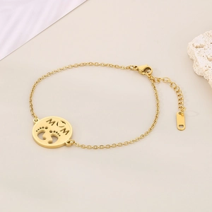 Detailed shot of golden MOM pendant bracelet with tiny baby footprints charm