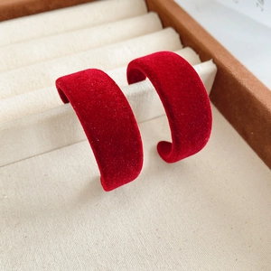 Close-up of red velvet C-shaped earrings on a beige display stand showing rich fabric texture