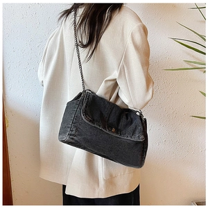 Detail of black denim tote bag with metal chain strap shown on a model back view