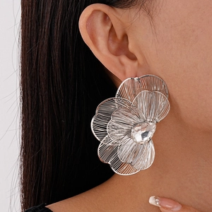 Detail of silver metallic flower earrings with crystal center on a model's ear