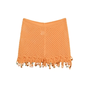 Detail of orange crochet beach skirt featuring colorful beadwork and fringe hemline