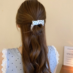 Close-up of a cream and black polka dot bow scrunchie styled on a woman's hair