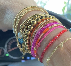 Close-up of stacked gold bead bracelets and pearl bangles with a heart charm on wrist