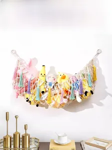 Handmade macrame toy hammock with colorful tassels displaying plush dolls on white wall
