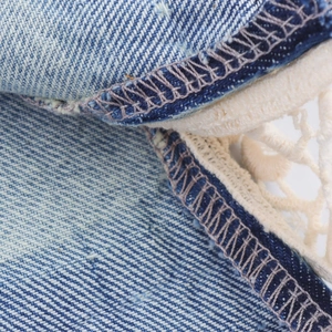 Macro detail of twill denim fabric with exquisite cream lace trim and reinforced stitching