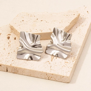Macro detail of silver irregular crumpled square earrings on beige travertine stone