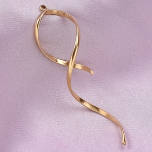 Detailed macro view of a golden ribbon-shaped spiral pendant on a purple textured fabric
