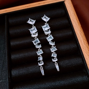 Détail de boucles d'oreilles pendantes argentées avec zircons carrés dans un coffret