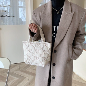 Detail of white quilted tote bag with brown rabbit print held by a model in a cafe