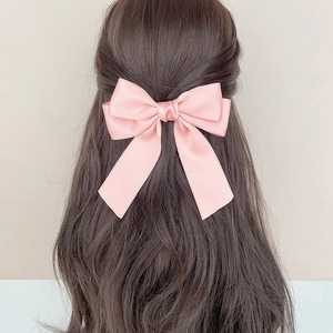 Pink satin bow hair clip with ribbons shown on long brown hair in a half-up style