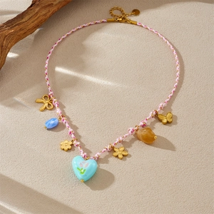 Collier en corde tressée avec cœur bleu et breloques de fleurs dorées sur fond beige
