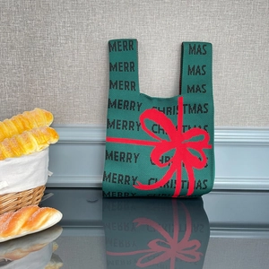 Gros plan d'un sac de Noël en tricot vert avec nœud rouge et texte de Noël
