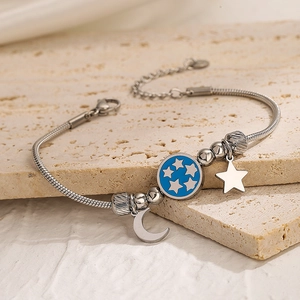 Titanium steel bracelet with blue enamel star and moon charms on textured stone background