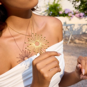 Close-up of a gold sunflower pendant necklace with artistic shadow effect on a model