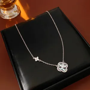 Collier trèfle argenté avec pendentif en zircon bleu posé sur un écrin à bijoux