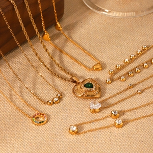 Détail de colliers dorés avec pendentifs en cœur et pierres vertes sur du lin