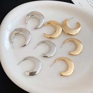 Detailed view of C-shaped gold and silver metallic earrings on a white ceramic tray