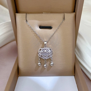 Detail of silver long life lock necklace with bells in a beige jewelry box on white satin