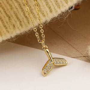 Collana con ciondolo a coda di pesce in zircone dorato su sfondo in maglia beige