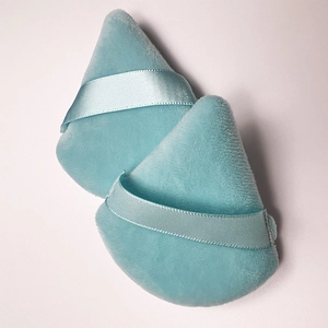 Close-up of two blue triangular velvet powder puffs with satin ribbon handles for makeup