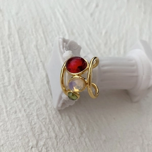 Detailed view of adjustable gold ring with red white and green crystal stones
