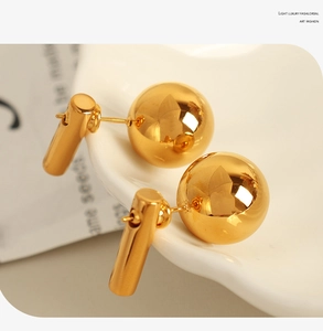 Close-up of high-polish 18k gold plated titanium steel ball earrings on a white ceramic tray