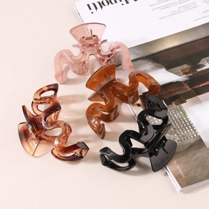 Set of four wavy resin hair claws in pink, amber, brown and black on a beige table