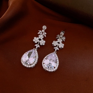 Close-up of silver pear-shaped zircon drop earrings on elegant brown silk fabric