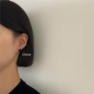 Close-up of 10mm black round stud earrings worn on the ear showing elegant scale