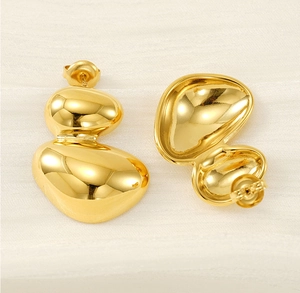 Détail de boucles d'oreilles dorées géométriques irrégulières sur tissu blanc