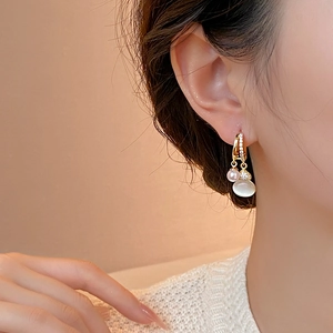 Close-up of golden gourd opal and pearl drop earrings worn with crystal accents