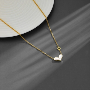 Golden heart necklace with white shell pendant and small letter e on a white plate