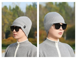 Close-up of light grey knit winter hat featuring ear flaps, short brim, and woven label detail