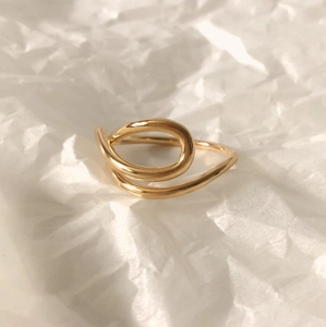 Detail of a minimalist gold knot ring with polished finish on white textured paper