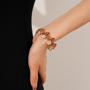 Nahaufnahme einer Dame mit goldenem Emaille-Blütenarmband und roten Blumenperlen