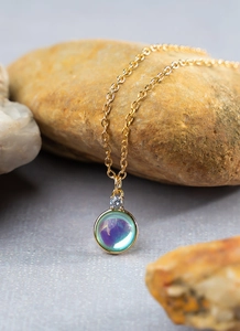Macro detail of round iridescent gemstone pendant with zircon on a gold chain