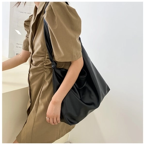 Side view of woman wearing large black PU leather tote bag in a minimalist indoor setting