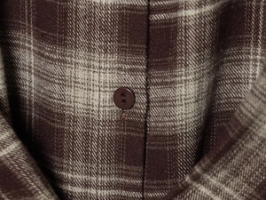 Macro detail of brown plaid shirt showing textured fabric and dark coffee buttons