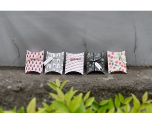 Five assorted mini pillow gift boxes with floral patterns and ribbon bows on a stone surface